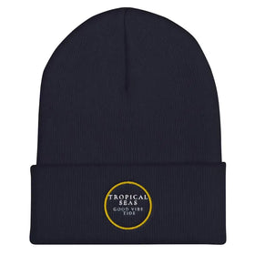 Navy blue knit beanie with a folded cuff and embroidered circular logo in gold thread reading ’tropical seas good vibe tide.’