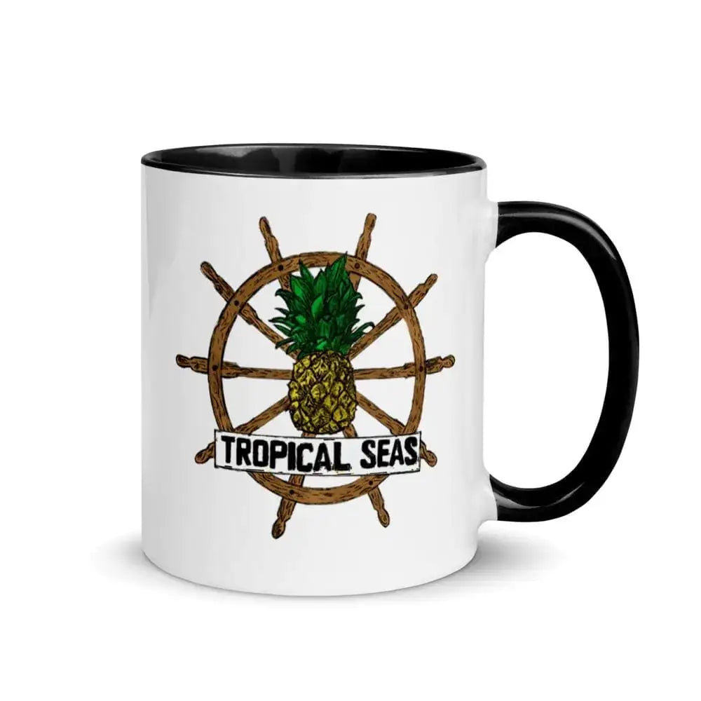 White ceramic mug with black rim and handle, featuring a tropical-themed graphic of a pineapple centered on a wooden ship’s wheel with the text ’tropical seas’ below.
