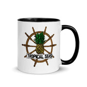 White ceramic mug with black rim and handle, featuring a tropical-themed graphic of a pineapple centered on a wooden ship’s wheel with the text ’tropical seas’ below.