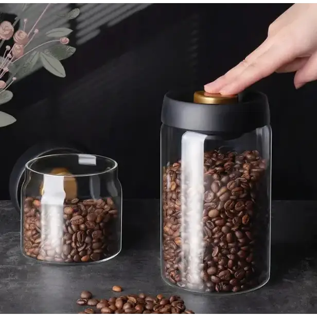 Clear glass coffee bean storage jar with a black lid and gold-colored knob.