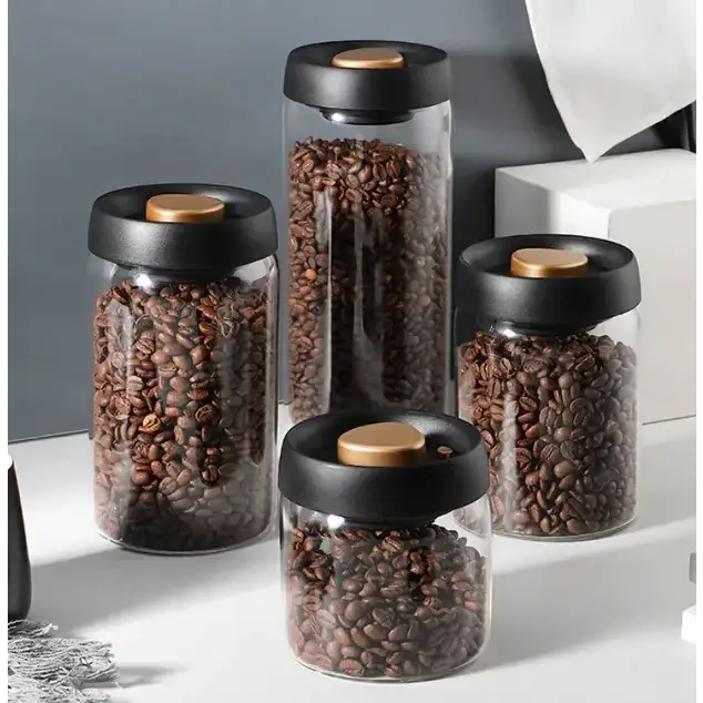 Set of four clear glass coffee bean storage jars with black lids and gold-toned inner seals.