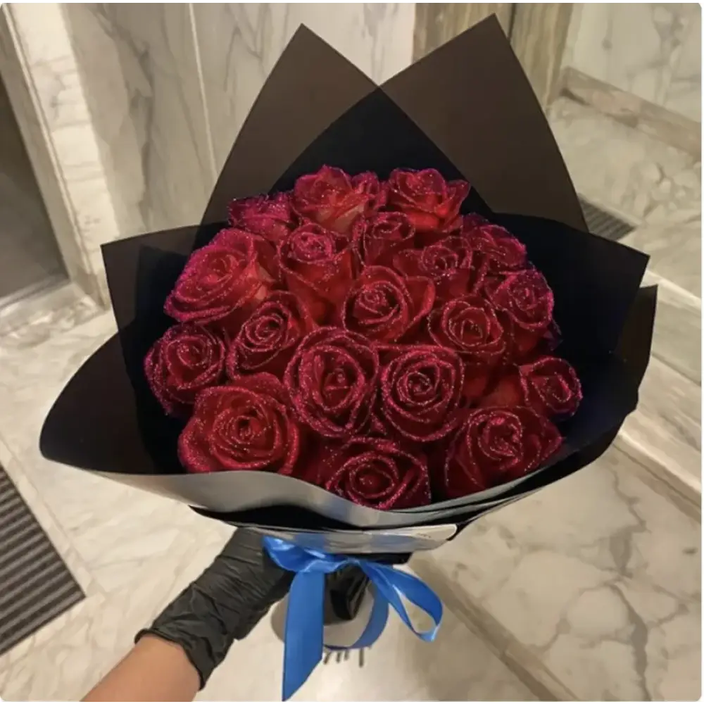 A bouquet of deep red, glitter-frosted roses wrapped in black paper and tied with a blue ribbon.
