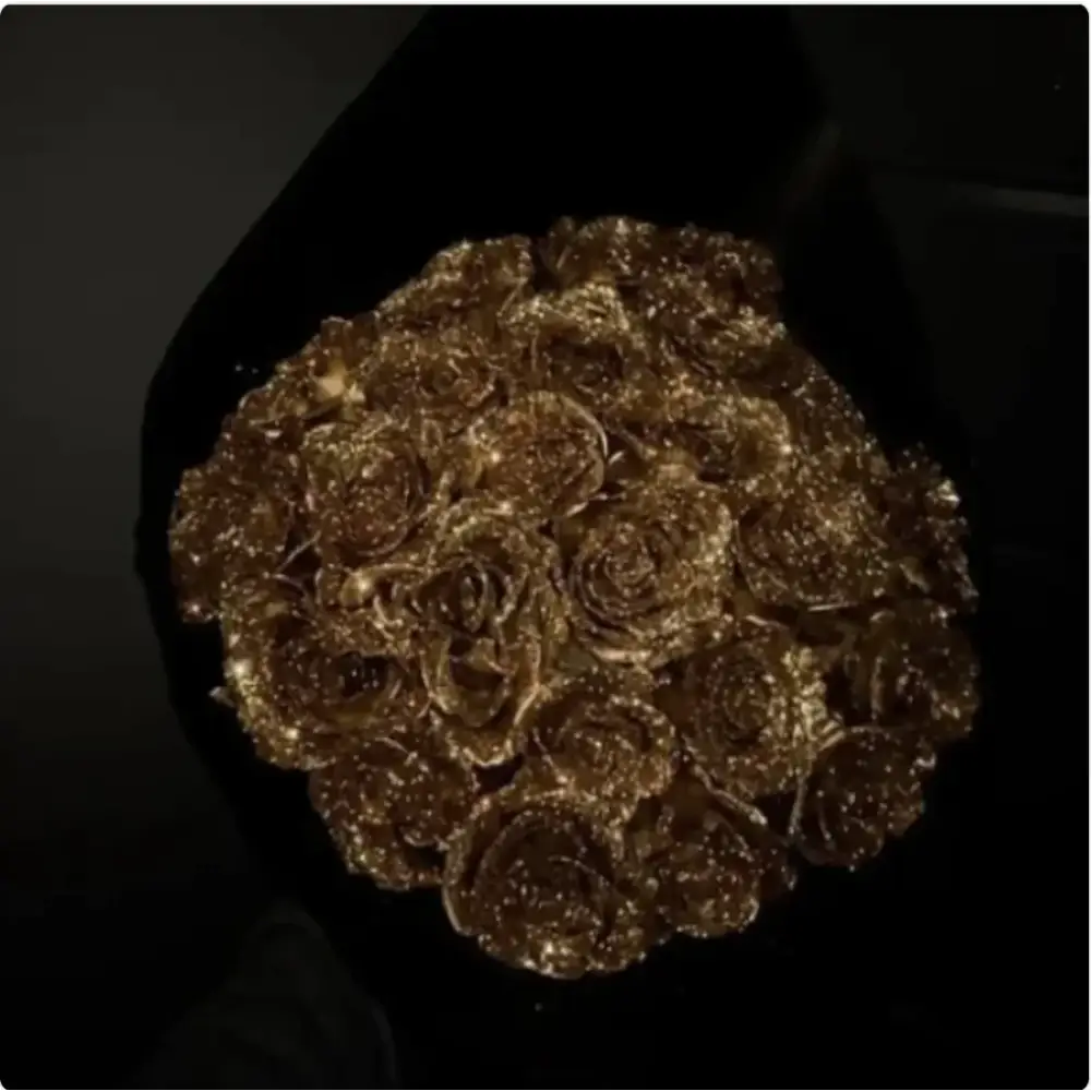 A bouquet of golden, glitter-dusted roses wrapped in black foliage.