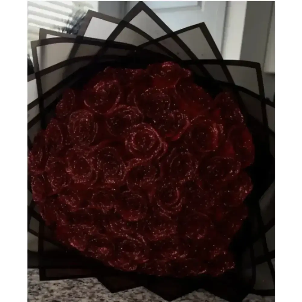 A lush bouquet of deep red, glittery roses wrapped in black geometric paper.