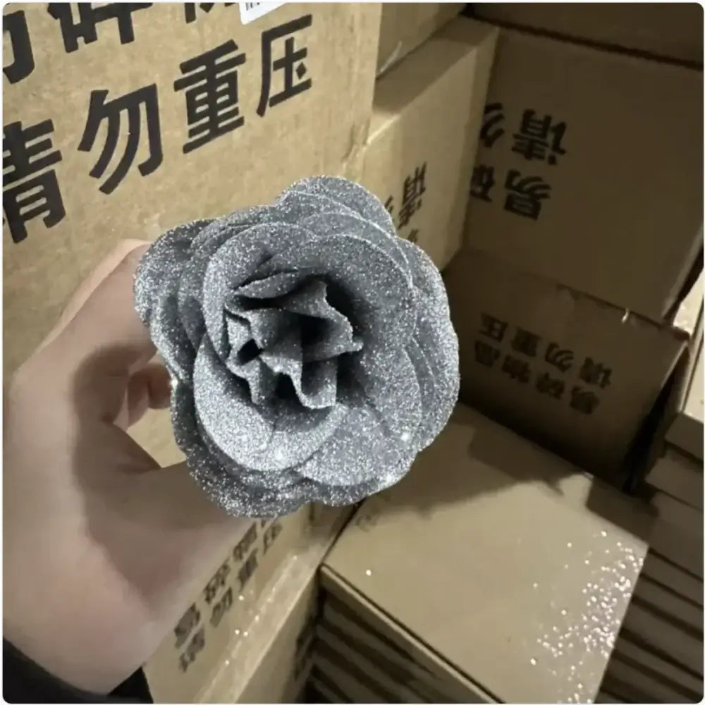 A glittery silver artificial rose with layered petals, crafted from a sparkly fabric material.