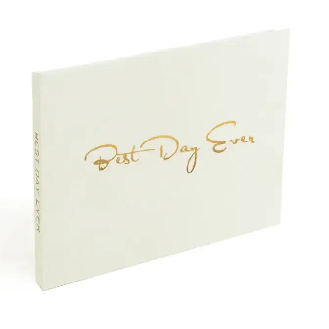 A cream-colored hardcover photo book with gold foil lettering that reads ’best day ever’ in a cursive script.