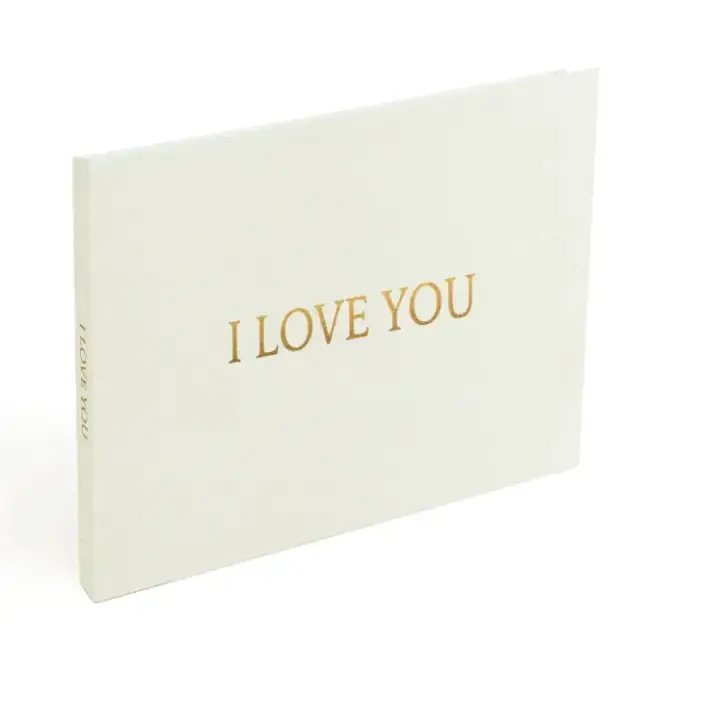 A cream-colored, soft-touch photo book with elegant gold foil lettering that reads ’i love you’ across the front cover.