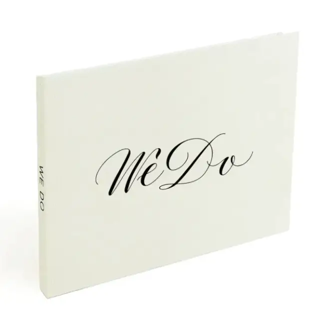 A minimalist off-white wedding guest book with elegant black cursive ’we do’ lettering on the cover.