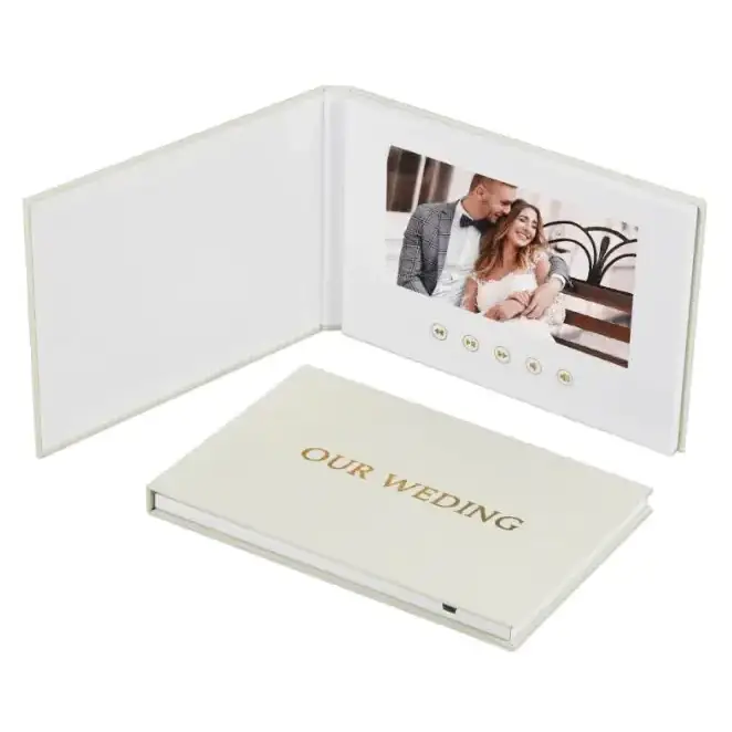 Cream-colored leather-bound digital photo book with a built-in screen displaying a couple’s wedding photo and gold-embossed ’our wedding’ on the cover.