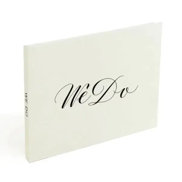Cream-colored wedding guest book with elegant black cursive ’we do’ lettering on the cover.