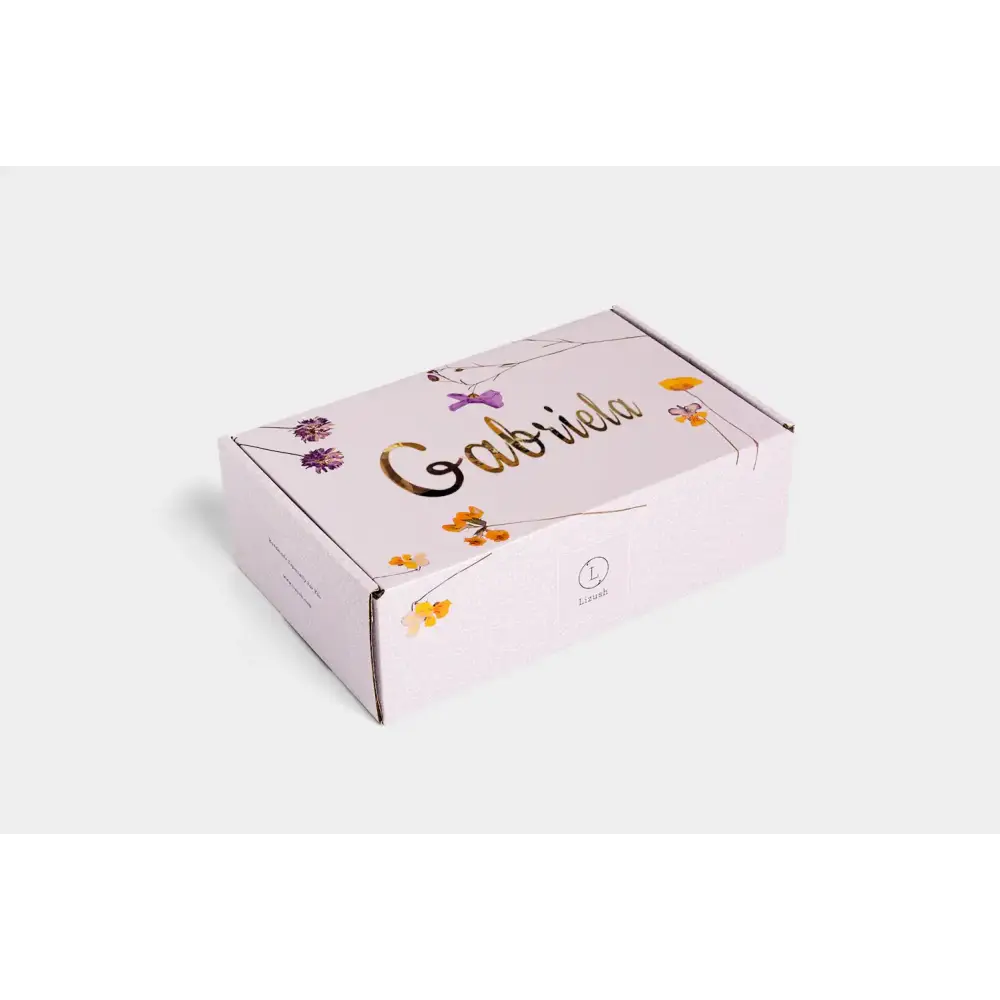 A delicate pink cardboard box adorned with a floral pattern and gold foil lettering that spells ’gabriela.’