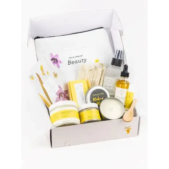 A white and yellow beeswax-based beauty kit with floral accents, featuring a branded pouch labeled ’you’re a natural beauty’ alongside various skincare products including jars of cream, bottles of oil, and candles.