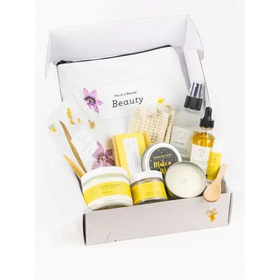A white and yellow beeswax-based beauty kit with floral accents, featuring a branded pouch labeled ’you’re a natural beauty’ alongside various skincare products including jars of cream, bottles of oil, and candles.