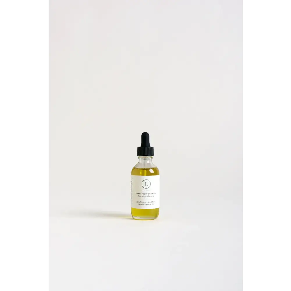 A clear glass bottle with a black dropper cap contains golden-yellow grape seed body oil, labeled ’nourishing & moisturizing’ on its white label.