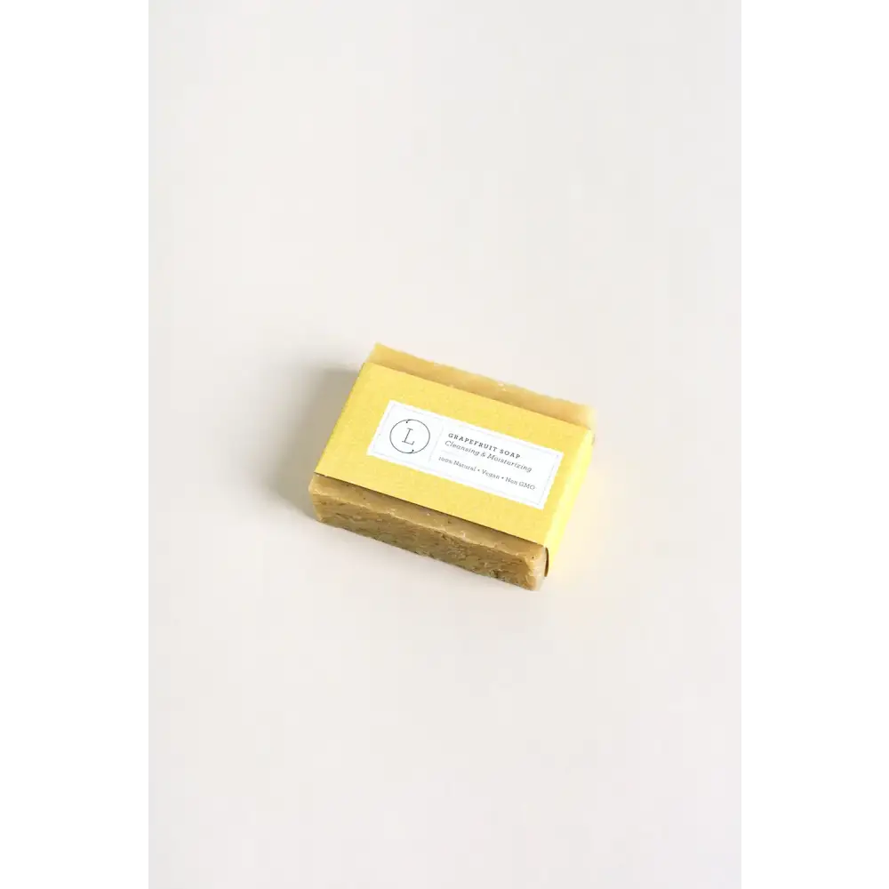 A rectangular bar of pale yellow grapefruit soap with a matte finish, wrapped in matching yellow paper and labeled ’grapefruit soap’ by l.