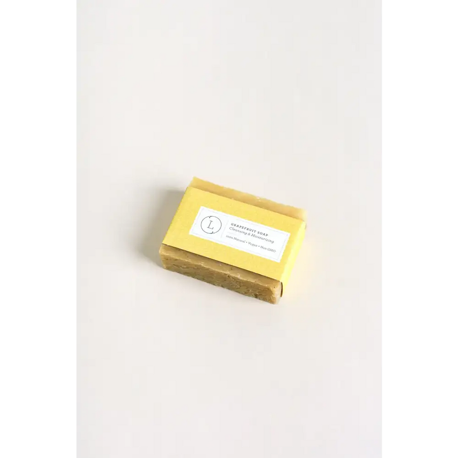 A rectangular bar of pale yellow grapefruit soap with a matte finish, wrapped in matching yellow paper and labeled ’grapefruit soap’ by l.