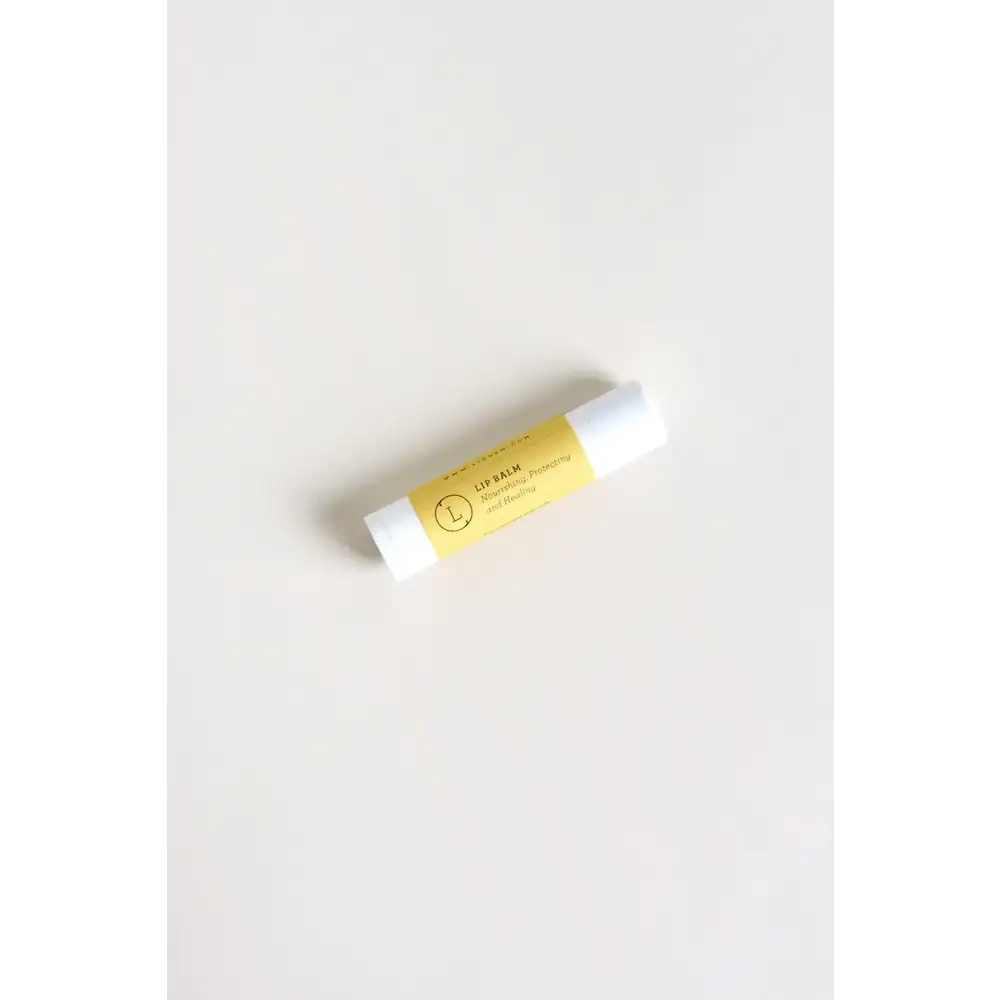 A sleek white lip balm tube with a vibrant yellow label featuring elegant black text and a minimalist circular logo.
