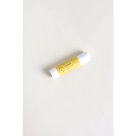 A sleek white lip balm tube with a vibrant yellow label featuring elegant black text and a minimalist circular logo.