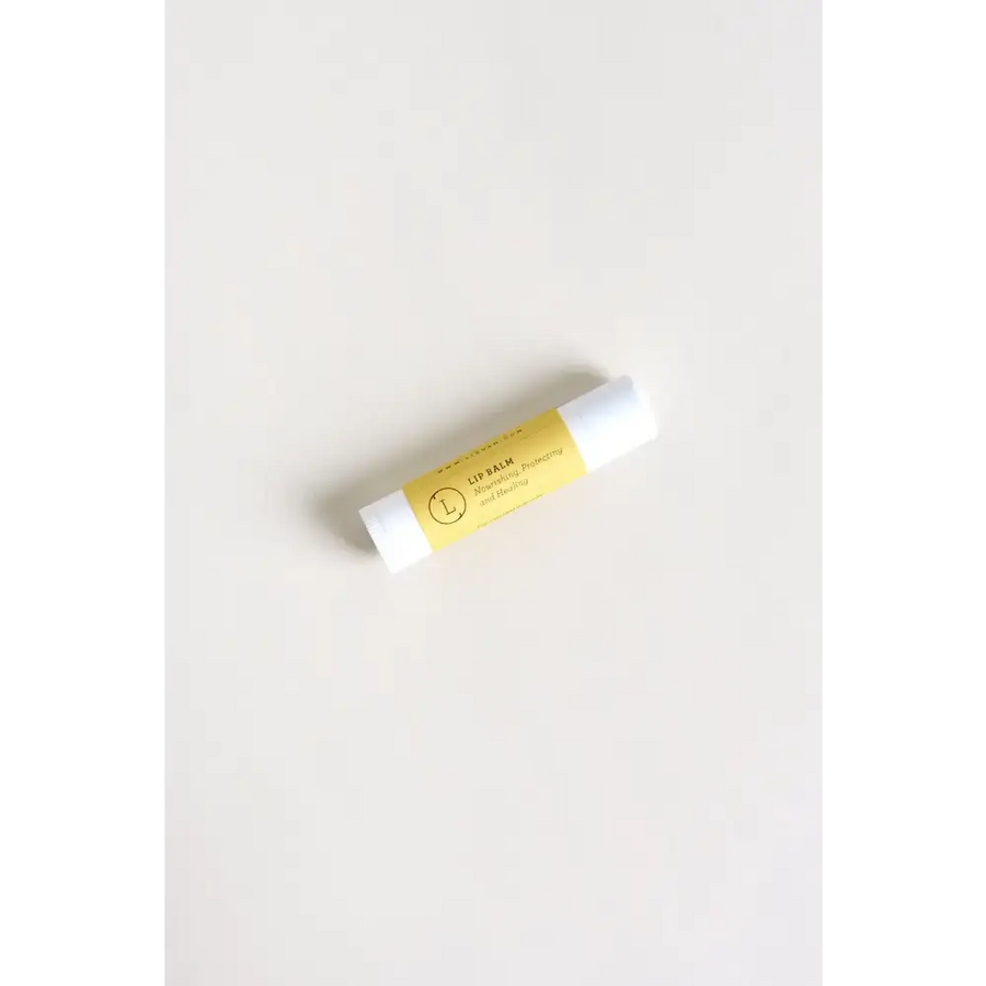 A sleek white lip balm tube with a vibrant yellow label featuring elegant black text and a minimalist circular logo.