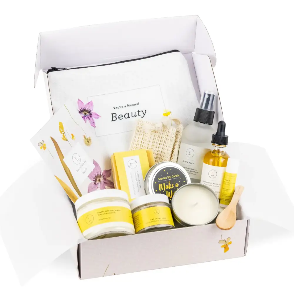 A white and yellow natural beauty gift set box containing candles, lotions, oils, a scrubber, and floral-themed accessories.