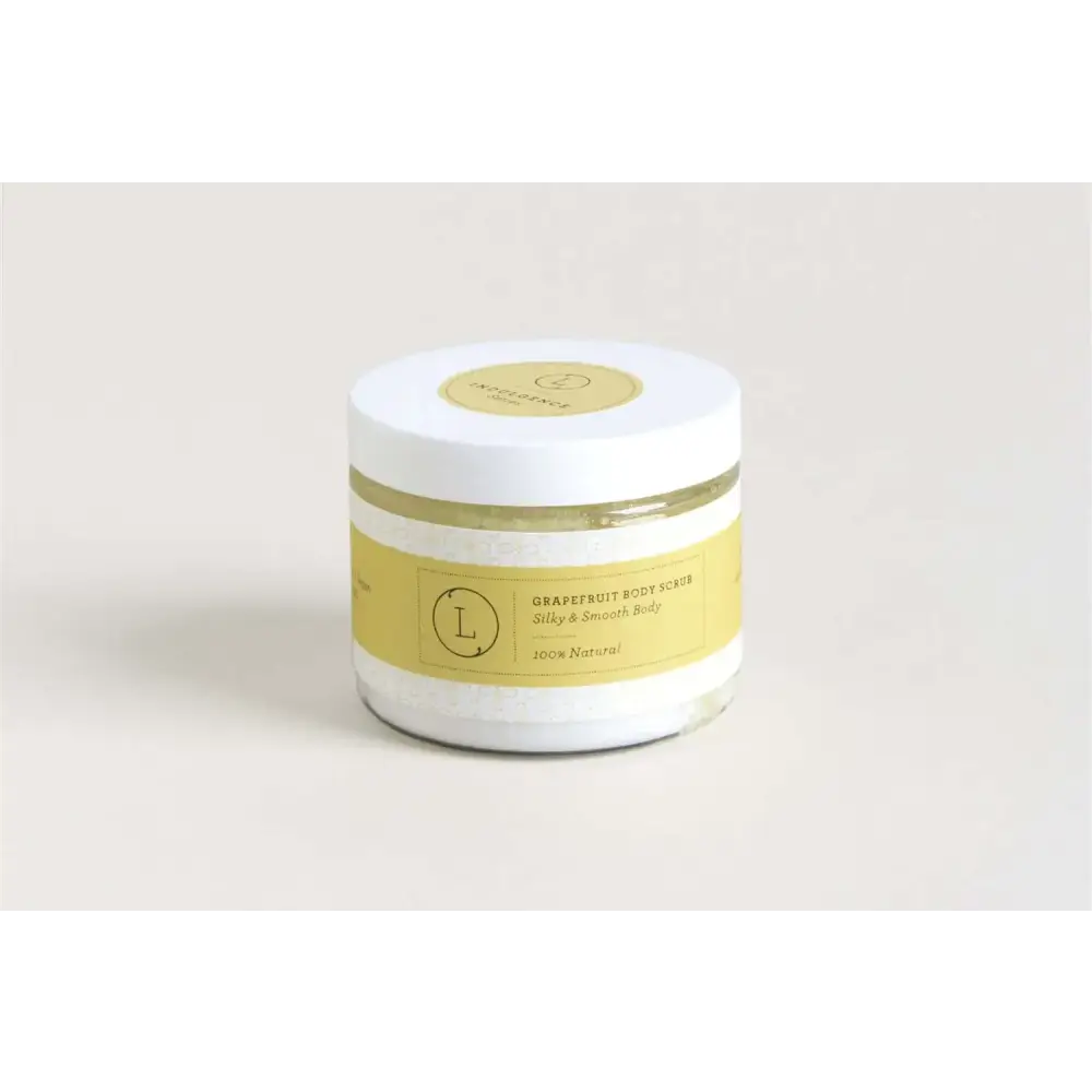 A white glass jar with a yellow label and lid, containing a grapefruit body scrub.