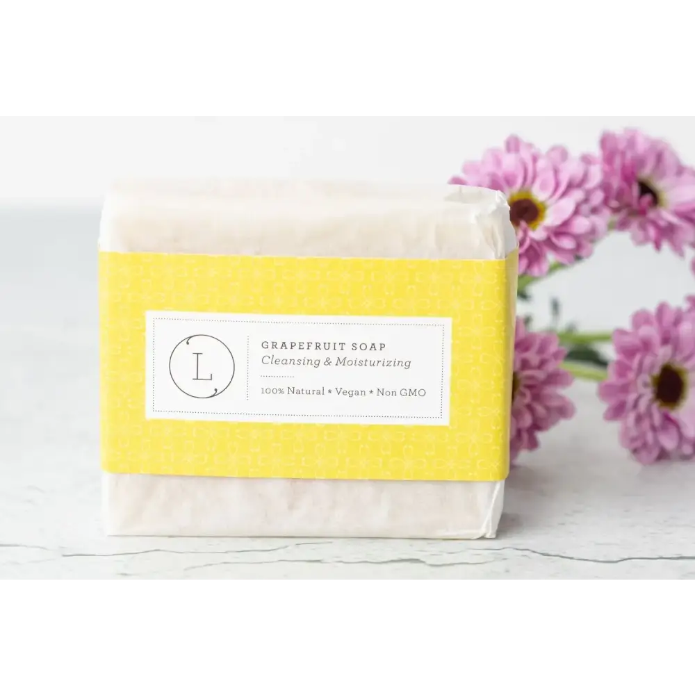 A rectangular bar of pale yellow grapefruit soap wrapped in a bright yellow paper label with black text and a circular logo.
