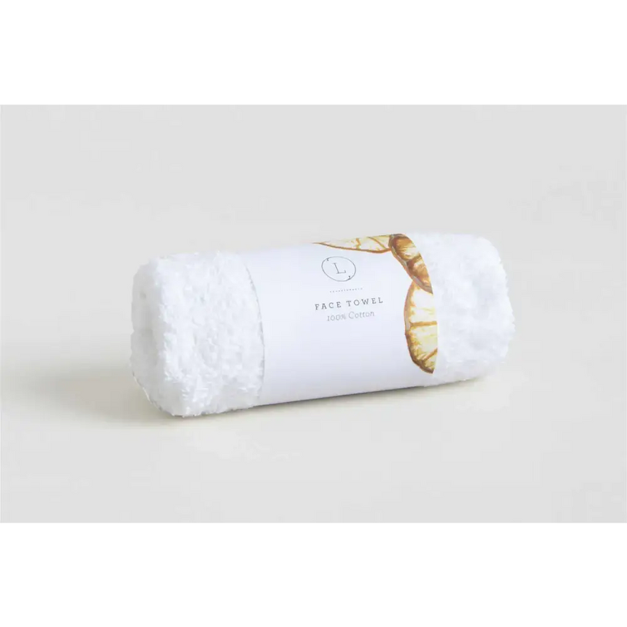 A plush white cotton face towel, neatly rolled and wrapped with a minimalist label featuring gold-toned leaf accents.