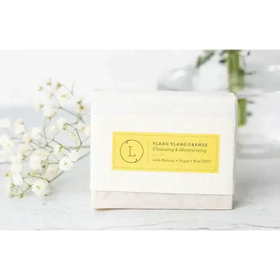 A white rectangular bar of soap with a yellow label that reads ’ylang ylang orange cleansing & moisturizing’ and features a circular logo.
