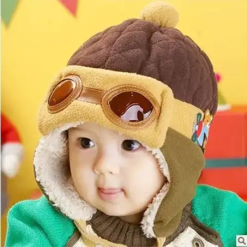 Brown knitted pilot hat with tan faux leather goggles and fluffy pom-pom