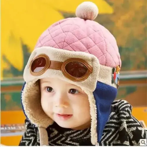 Pink quilted baby hat with a fluffy pom-pom, beige fleece trim and blue ear flaps.