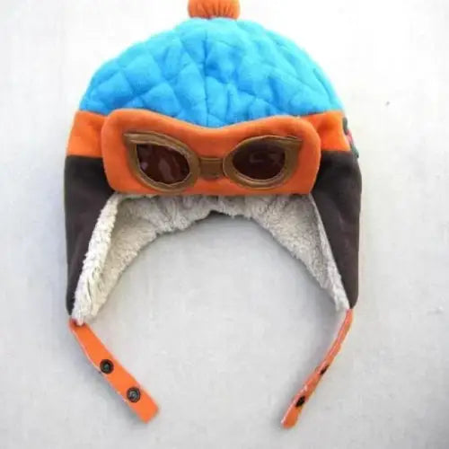 A vibrant blue quilted winter hat with orange and black accents, featuring a built-in pair of goggles and fluffy ear flaps.