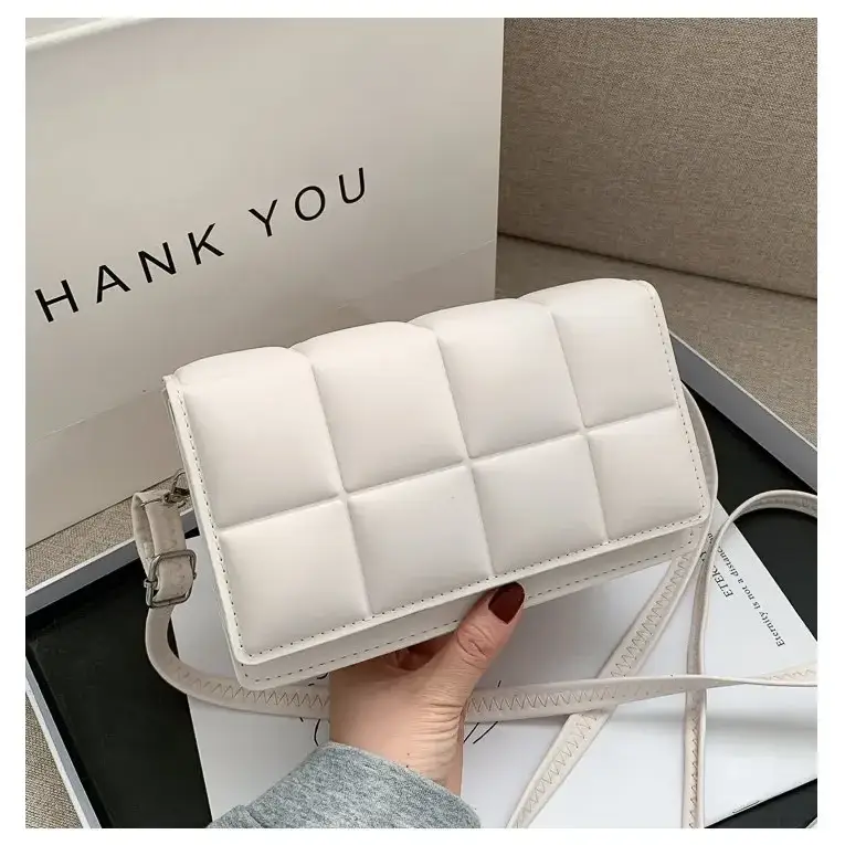 A white quilted crossbody bag with a textured, padded design and matching strap.