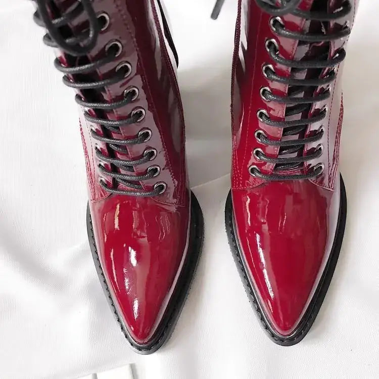 A pair of glossy crimson patent leather lace-up ankle boots with black laces and a pointed toe.
