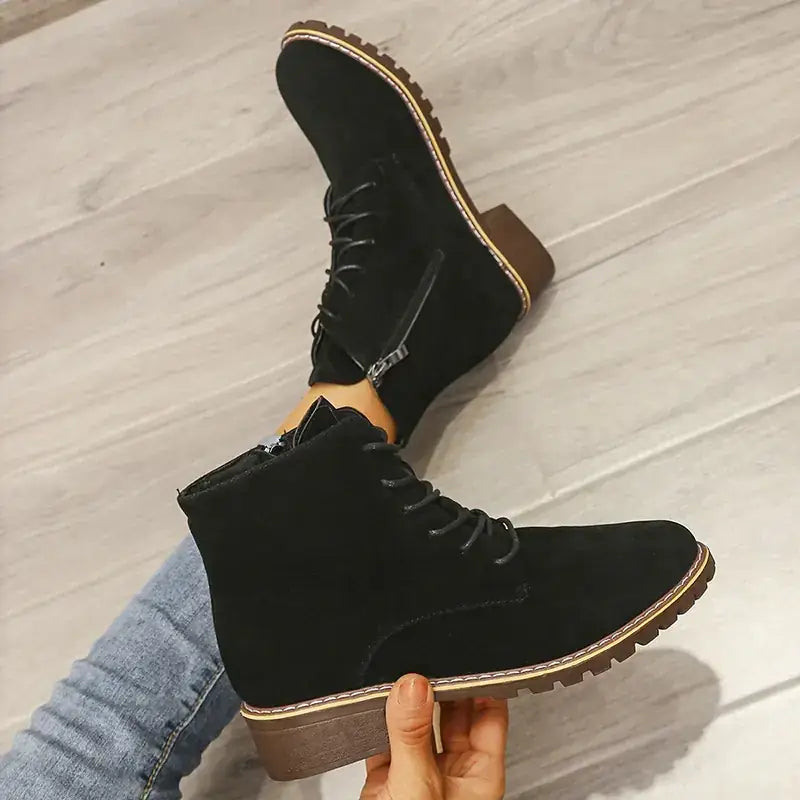 Black suede ankle boots with a chunky brown heel and contrasting tan stitching along the sole edge.