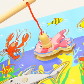 A wooden fishing game featuring a pink and yellow striped fish with googly eyes, attached to a red string and hanging from a light-colored wooden rod.