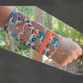 A vibrant orange zipper runs along the side of a fabric wristband featuring an intricate paisley pattern in shades of red, teal, and white.